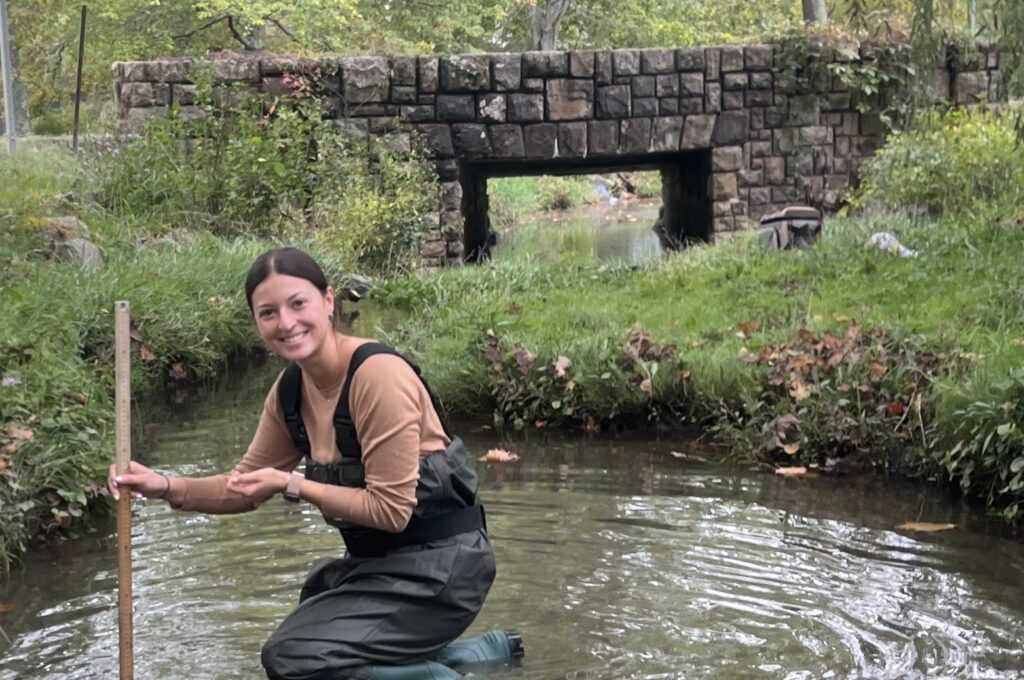 Andie Flota is taking samples in a stream. 